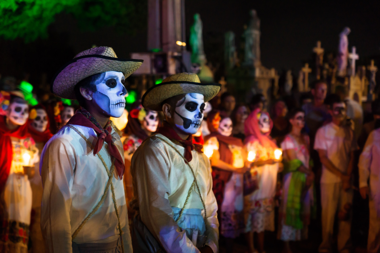 Two customed cowboys with skull make-up in front of a line of costumed people with candles and graveyard at the event for dias de los muertos at the Festival Des Las Animas at the Cementerio General, Merida, Mexico